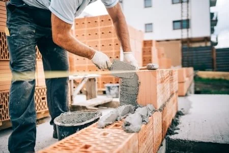 Ein Handwerker verteilt Mauermörtel auf einer Mauer aus Mauersteinen